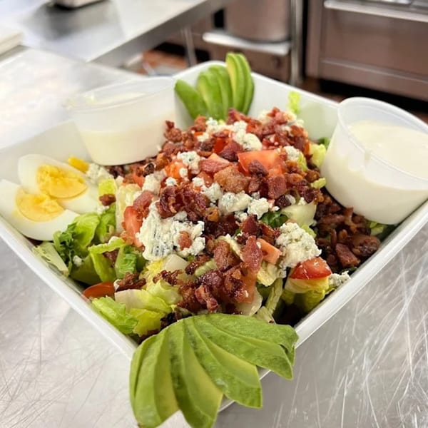 A vibrant La Bella Vita Kitchen and Bar salad with lettuce, bacon, blue cheese, tomatoes, avocado, and eggs.