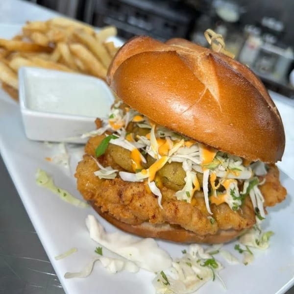 Crispy fried chicken sandwich with coleslaw, pickles, and sauce, served with fries and dip.
