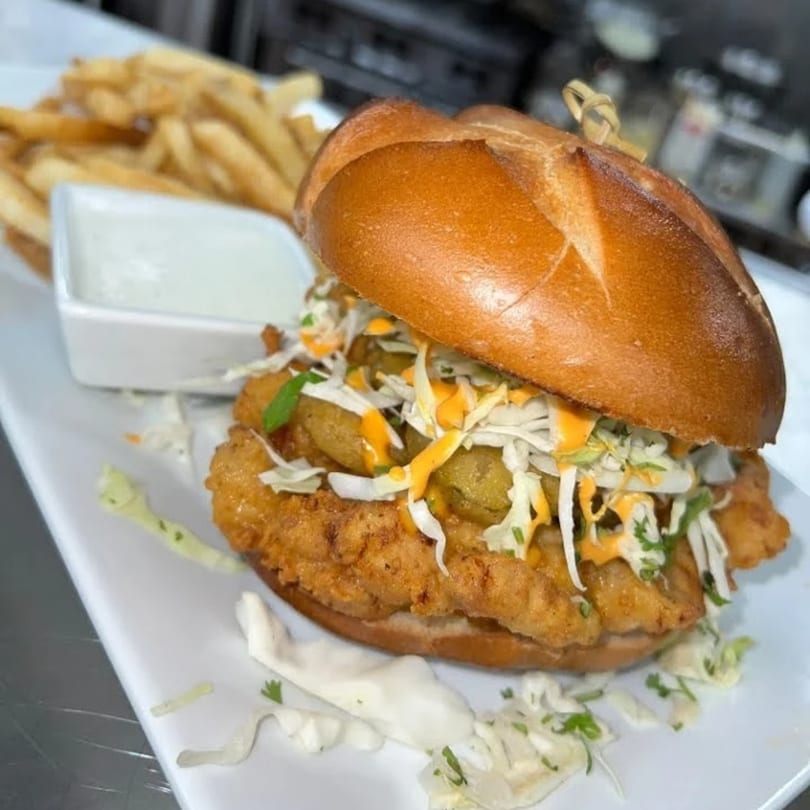 Crispy fried chicken sandwich with coleslaw, pickles, and sauce, served with fries and dip.
