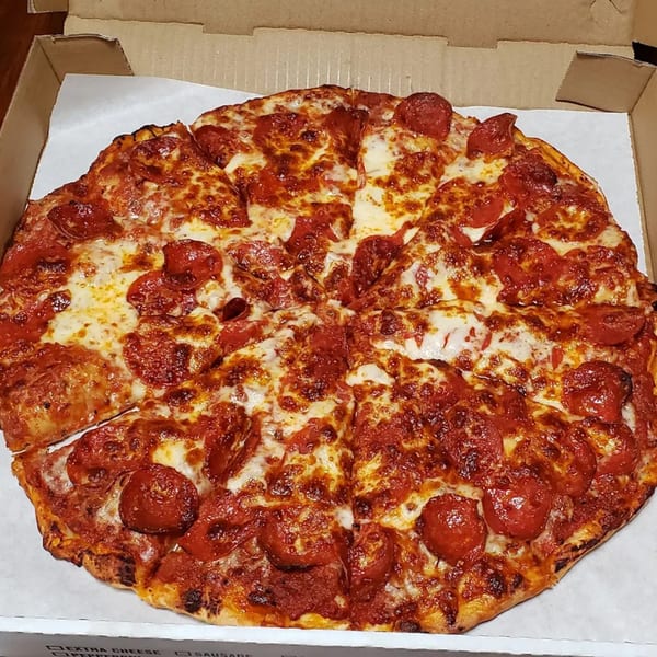 A whole pepperoni pizza, sliced and ready to eat, in a cardboard delivery box.