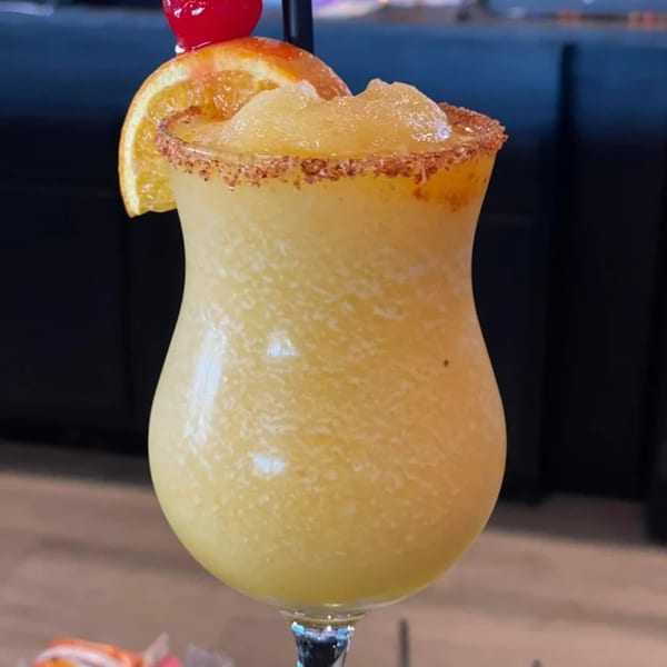 Frozen yellow drink in a hurricane glass, garnished with an orange slice and cherry.