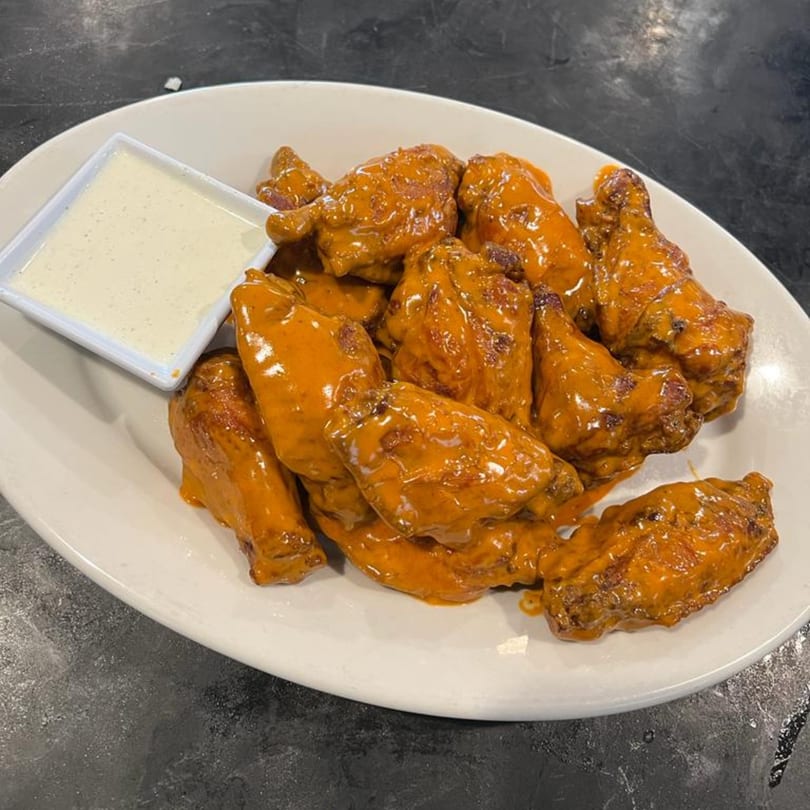 A plate of buffalo chicken wings with a side of ranch dressing on a dark table.