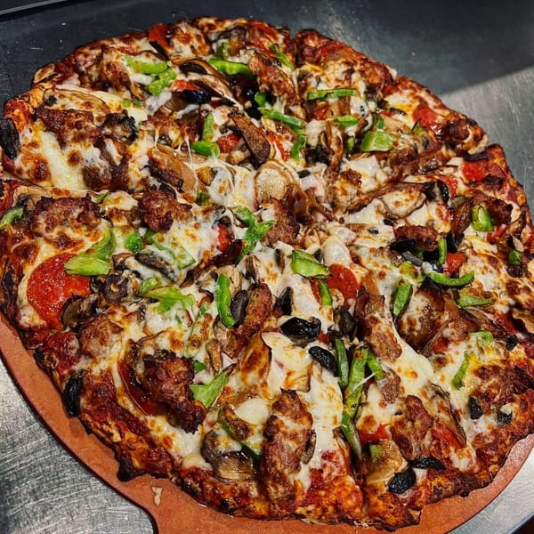 A large, hot La Bella Vita Kitchen and Bar pizza with various toppings on a wooden peel.
